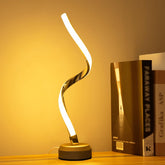 Modern table lamp with a curved design on a wooden surface next to books.